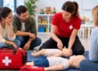 Instructora de primeros auxilios mostrando técnicas de atención a un bebé con un maniquí de entrenamiento, mientras varios alumnos observan durante un curso de primeros auxilios infantiles.